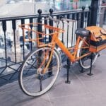 Pomarańczowy rower z torbą dostawczą stoi w pomieszczeniu