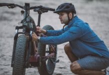 Co może się zepsuć w rowerze elektrycznym w podróży i jak się na to przygotować Mężczyzna w kasku naprawia rower elektryczny na piaszczystym szlaku