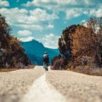 Rowerzysta jedzie wiejską drogą, w tle góry i błękitne niebo