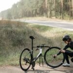 Rowerzysta naprawiający koło roweru przy leśnej, wiejskiej drodze