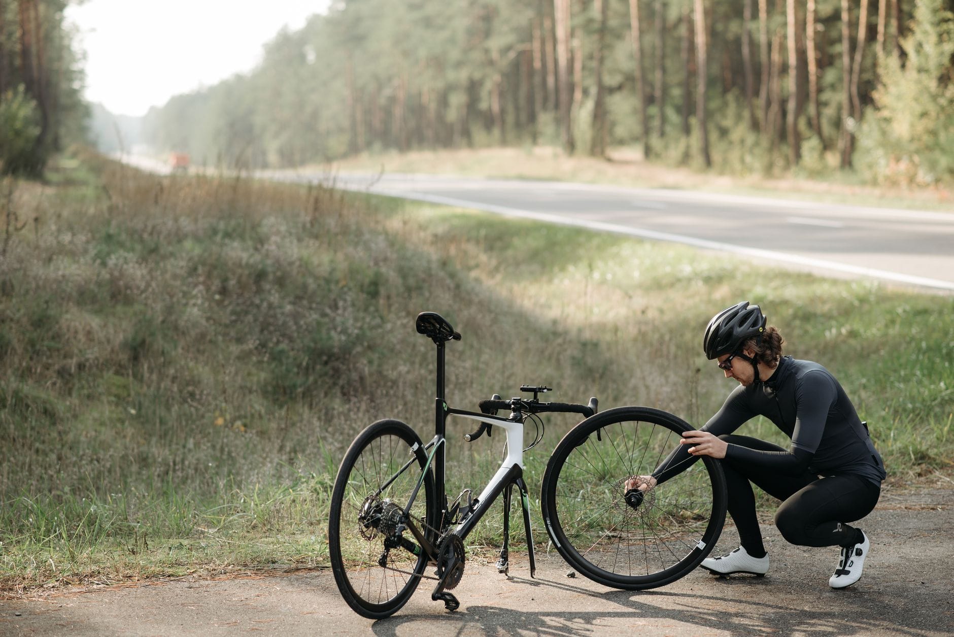 Rowerzysta naprawiający koło roweru przy leśnej, wiejskiej drodze
